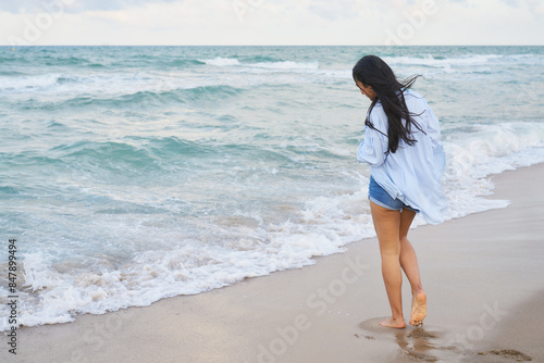 A woman is walking on the beach wearing a white shirt and blue shorts photo