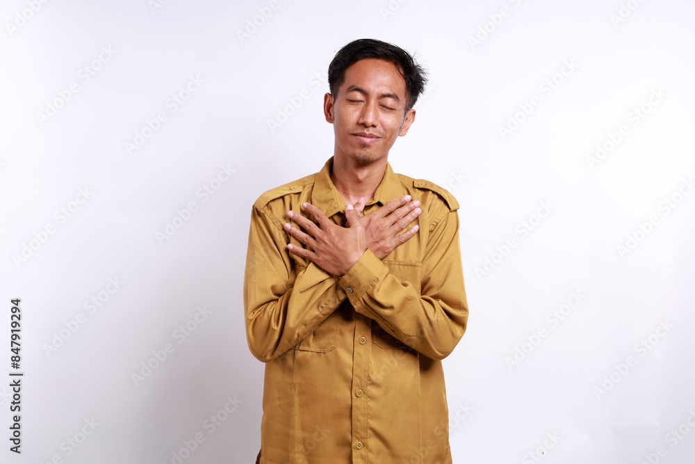 Relieved Indonesian government employees standing while holding chest. He feels peaceful Relieved Indonesian government employees standing while holding chest. He feels peaceful
