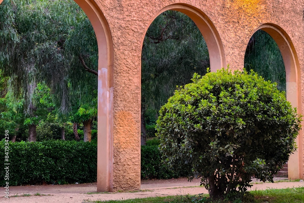Fototapeta premium Serene park scene featuring an archway with lush green trees and bushes.