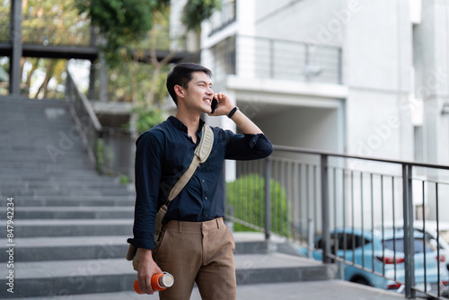 Businessman Walking Outdoors Holding Reusable Eco-Friendly Cup, Talking on Phone, Promoting Sustainable Lifestyle and Eco-Friendly Practices in Urban Environment