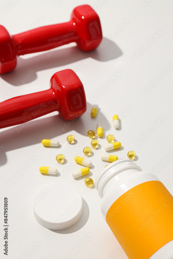 Plastic jar with vitamins and red dumbbells on white background Plastic jar with vitamins and red dumbbells on white background