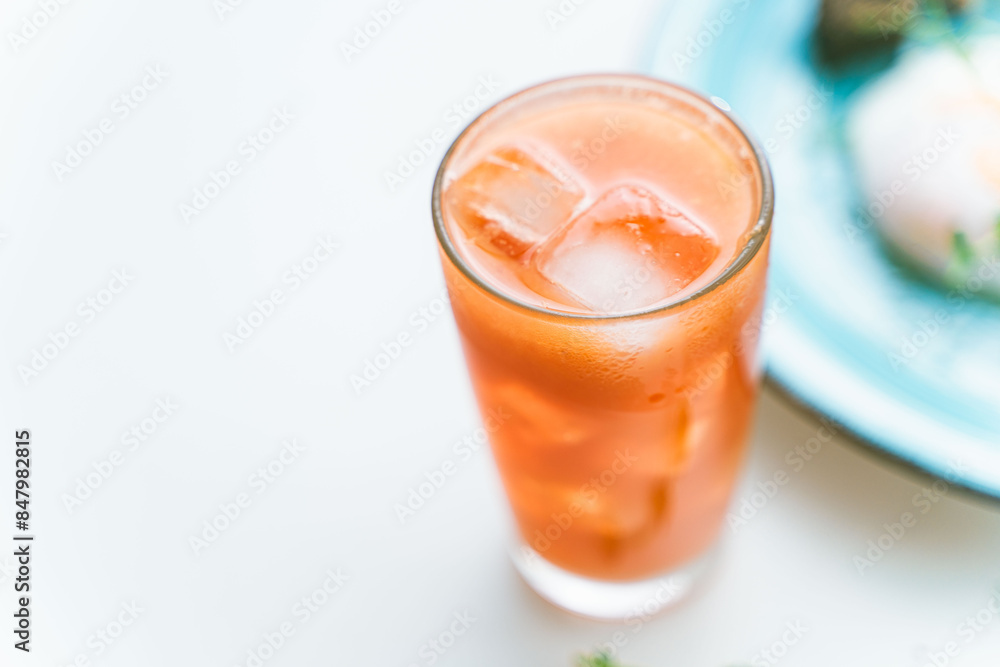 Fototapeta premium Grapefruit freshly squeezed juice with ice in a glass glass on a white background, chosen trick. A place to copy a space