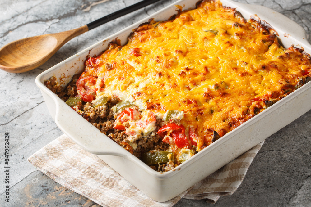 Classic John Wayne casserole has wonderfully southwest flavors, ground beef, a biscuit crust, fresh tomatoes, and a cheesy creamy topping closeup on the baking dish on the table. Horizontal