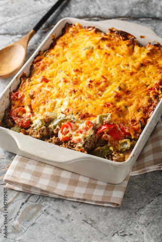 John Wayne Casserole is a delicious taco beef casserole cooked in biscuit dough with sour cream, Cheddar cheese, tomatoes, and bell peppers closeup on the baking dish on the table. Vertical photo