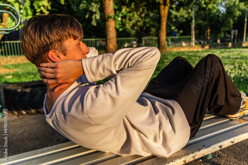 Young Man Doing Sit-Ups on Park Bench in Summer Sunlight