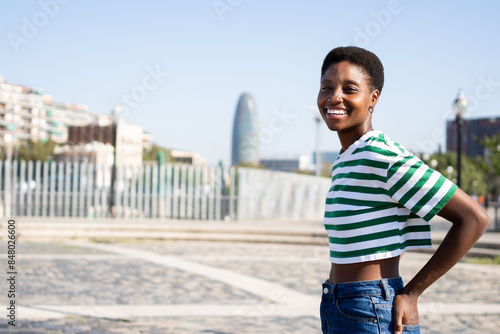 Canvas Print Young African woman with short afro hairstyle smiling standing in Barcelona city