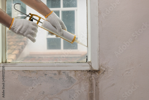 Construction worker using silicone sealant caulk for repair leaked inside window frame. photo