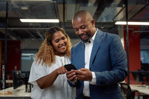 Two happy multiracial business people in businesswear using mobile phone in office