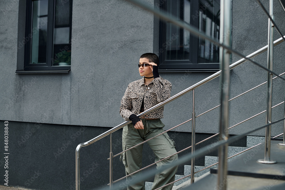A young woman in stylish attire with short hair descends a modern staircase near a leopard-print jacket-clad woman.
