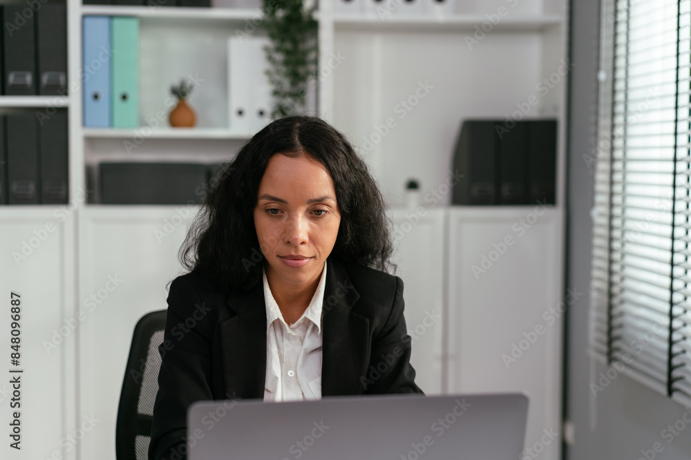 Latino business woman sitting at desk working with laptop, watching work project, reading e-mail, communicate with online customer in the office Latino business woman sitting at desk working with laptop, watching work project, reading e-mail, communicate with online customer in the office