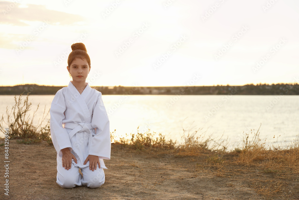 Cute little girl in kimono meditating near river at sunset. Karate practicing Cute little girl in kimono meditating near river at sunset. Karate practicing