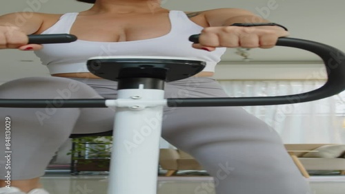 Vertical shot of Hispanic sportswoman using augmented reality glasses while exercising on fitness bike indoors