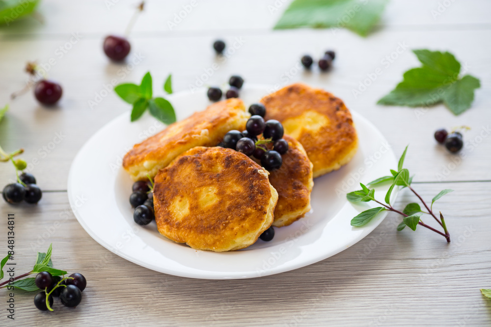 Fried curd cheese pancakes with black currants, on a wooden table Fried curd cheese pancakes with black currants, on a wooden table