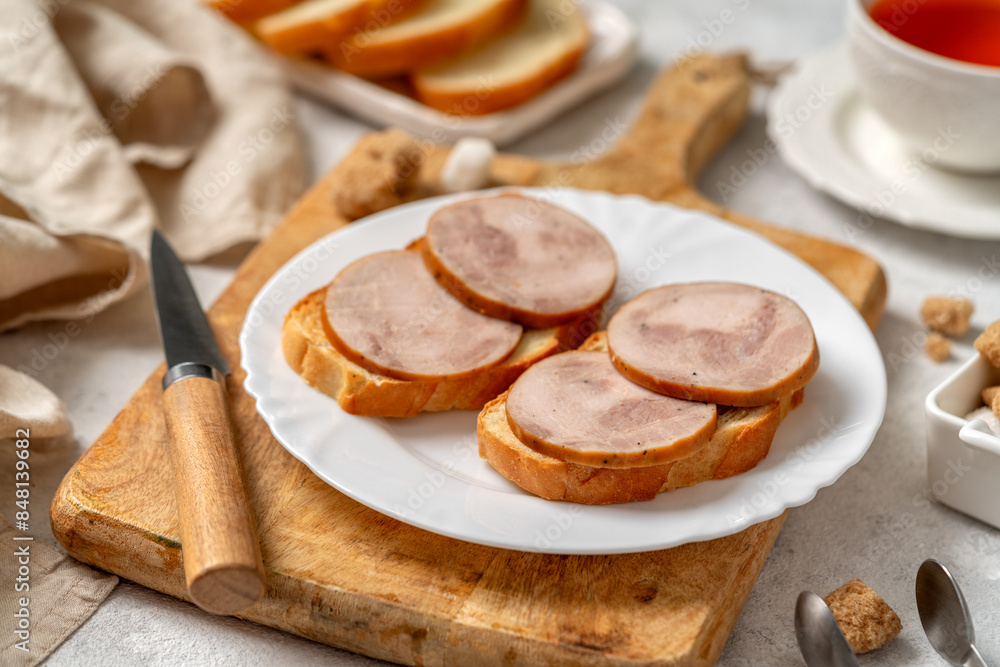 Bread with turkey ham in a white plate closeup. Toasts with sausage for breakfast on a bright table