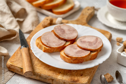 Obraz na płótnie Bread with turkey ham in a white plate closeup. Toasts with sausage for breakfast on a bright table w salonie