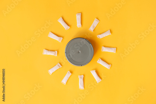 White thin snus sachets are laid out around a round jar on a yellow background.
