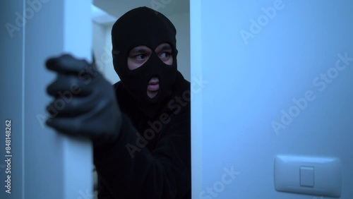 Close-up of a male thief with black mask opening the door to enter the room of apartment, home security to prevent the crimination, criminal impact on economic society.
 photo