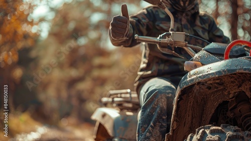 Person in camouflage gear rides ATV off-road, giving thumbs-up