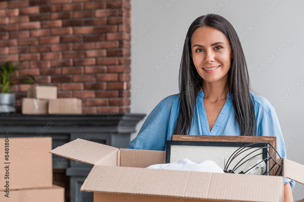 Young woman moving into new apartment holding cardboard box with stuff standing in living room. Delivery, relocation and unpacking, insurance, real estate, mortgage concept