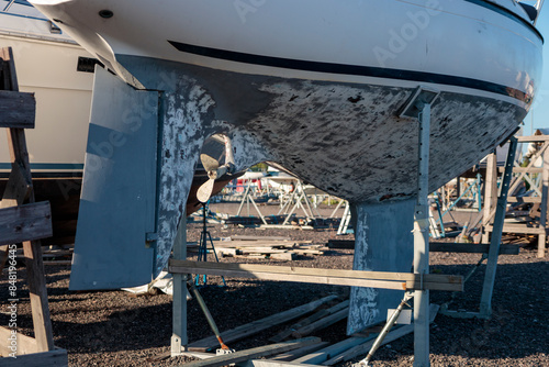 Boat painting, sanding, stripping of old paint from the surface of yacht, old boat ashore in a harbor boatyard for the winter storage and repair works before launchng