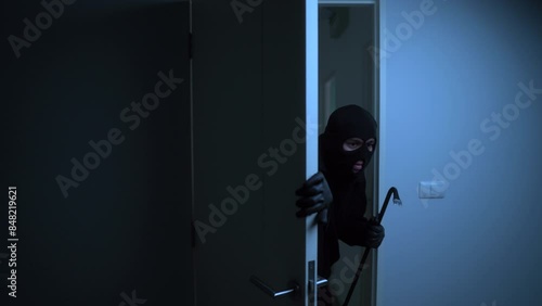 The male thief with black mask holding crowbar enter inside the room of apartment, home security to prevent the crimination, criminal impact on economic society.
 photo