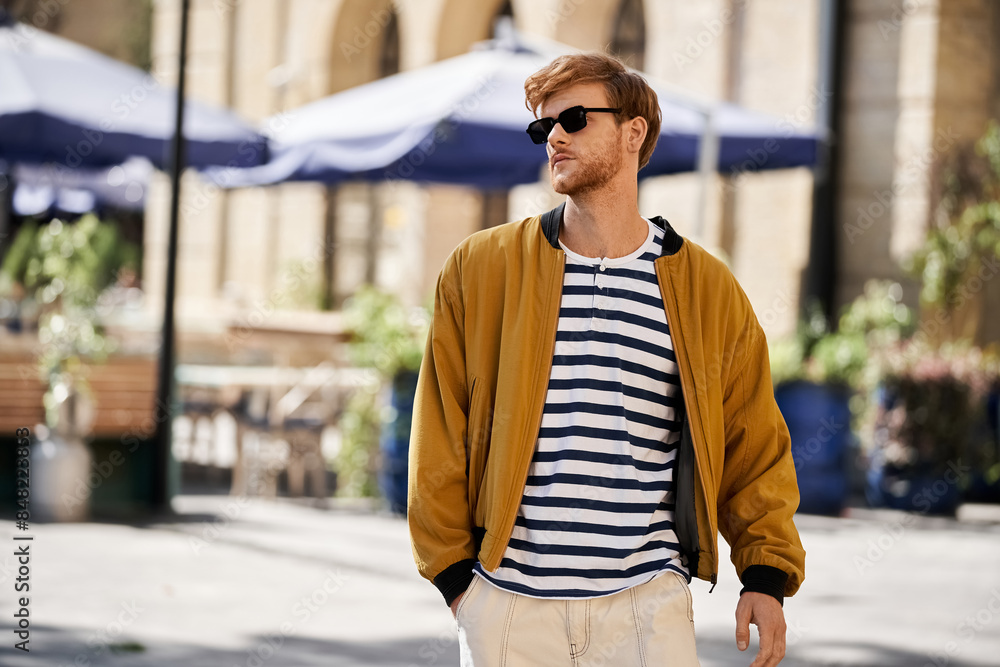 A fashionable red-haired man struts down the city street wearing stylish sunglasses. A fashionable red-haired man struts down the city street wearing stylish sunglasses.