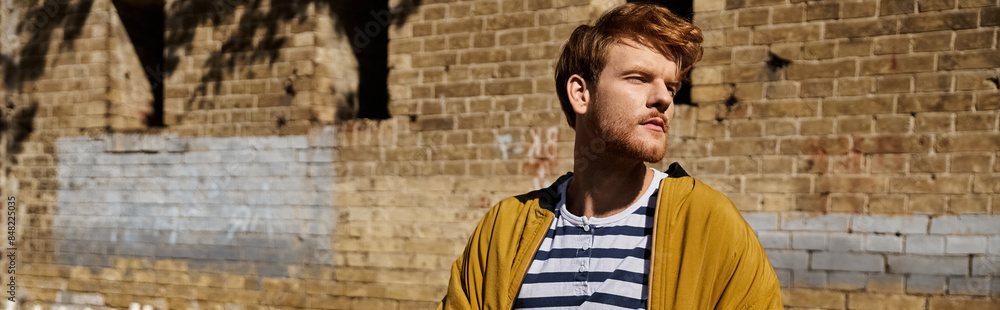A stylish young red-haired man standing confidently in front of a textured brick wall. A stylish young red-haired man standing confidently in front of a textured brick wall.