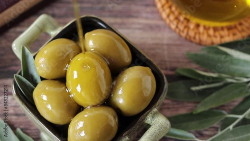 Pouring extra virgin olive oil on top of green olives. Close-up. Top view.