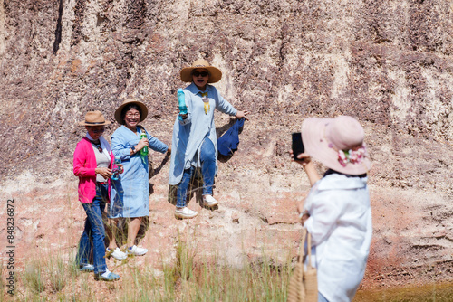 Elderly Asian women smiling and taking a selfie, enjoying nature by a lake. Dressed in casual outfits, sun hats, Capturing joyful moments, laughter, and friendship against a scenic backdrop.