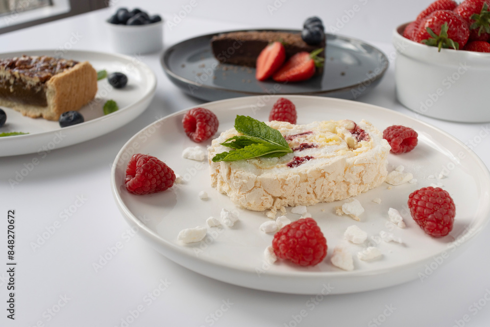 Plates with desserts close-up on a white background. Copy space. Pecan pie, meringue roll and chocolate cake are decorated with berries and mint leaves. Breakfast and tea Plates with desserts close-up on a white background. Copy space. Pecan pie, meringue roll and chocolate cake are decorated with berries and mint leaves. Breakfast and tea