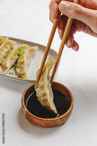 Hand taking gyoza dumpling from the plate with chopsticks, close-up view