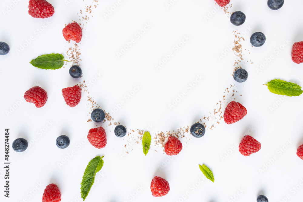 Berries and grated chocolate are laid out in the shape of a circle on a white background. Close-up, top view. Copy space. Pattern. Raspberries, blueberries and mint leaves for decoration Berries and grated chocolate are laid out in the shape of a circle on a white background. Close-up, top view. Copy space. Pattern. Raspberries, blueberries and mint leaves for decoration