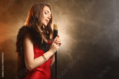 Beautiful young woman with microphone singing on color background with smoke, space for text