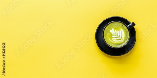 Elegant matcha latte in a black cup on a vibrant yellow background, showcasing detailed latte art for a fresh and modern coffee presentation.