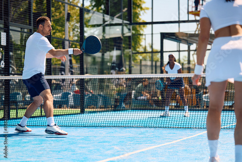 Athletic man in action during paddle tennis match in mixed doubles. © Drazen
