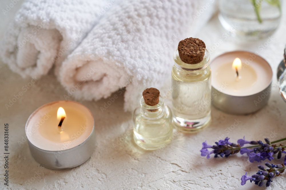 Transparent bottles of aromatherapy essential oil with lavender flowers, candles and spa treatment accessories Transparent bottles of aromatherapy essential oil with lavender flowers, candles and spa treatment accessories