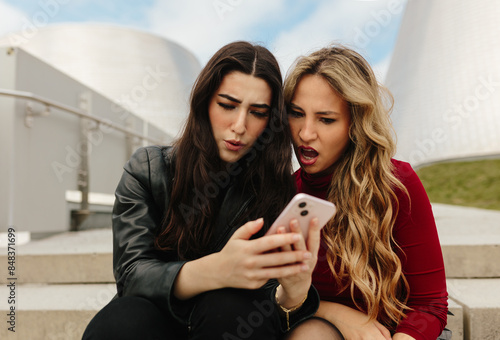 Two women reacting to smartphone content outdoors