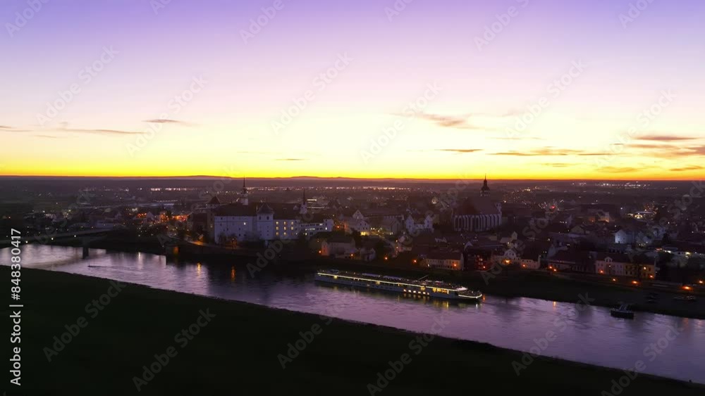 Flight towards Torgau at sunset. Dramatic sky over the city. Golden horizon line. Hartenfels Castle, the Elbe river and the city center beautifully illuminated. Flight towards Torgau at sunset. Dramatic sky over the city. Golden horizon line. Hartenfels Castle, the Elbe river and the city center beautifully illuminated.