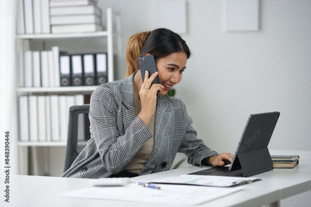 Businesswoman multitasking in modern office. Professional looking at laptop screen while talking on the phone, handling office work efficiently. Businesswoman multitasking in modern office. Professional looking at laptop screen while talking on the phone, handling office work efficiently.