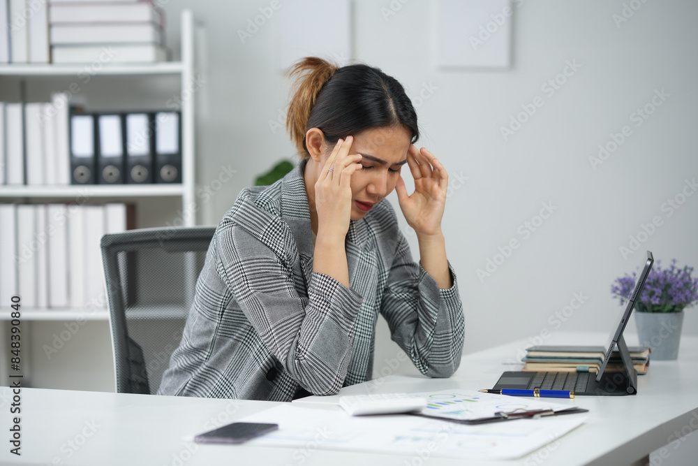 Stressed businesswoman holding head in hands while working at desk with paperwork and laptop in office. Stressed businesswoman holding head in hands while working at desk with paperwork and laptop in office.