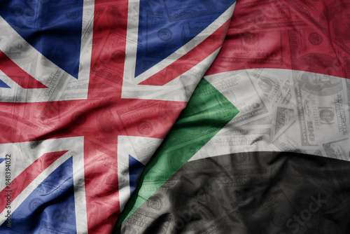 Canvas-taulu big waving colorful flag of sudan and national flag of great britain on the dollar money background
