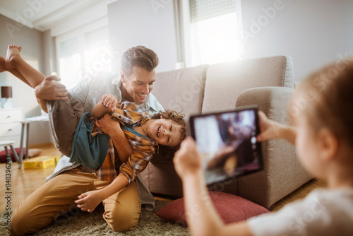 Father playing with son while being photographed by daughter at home photo