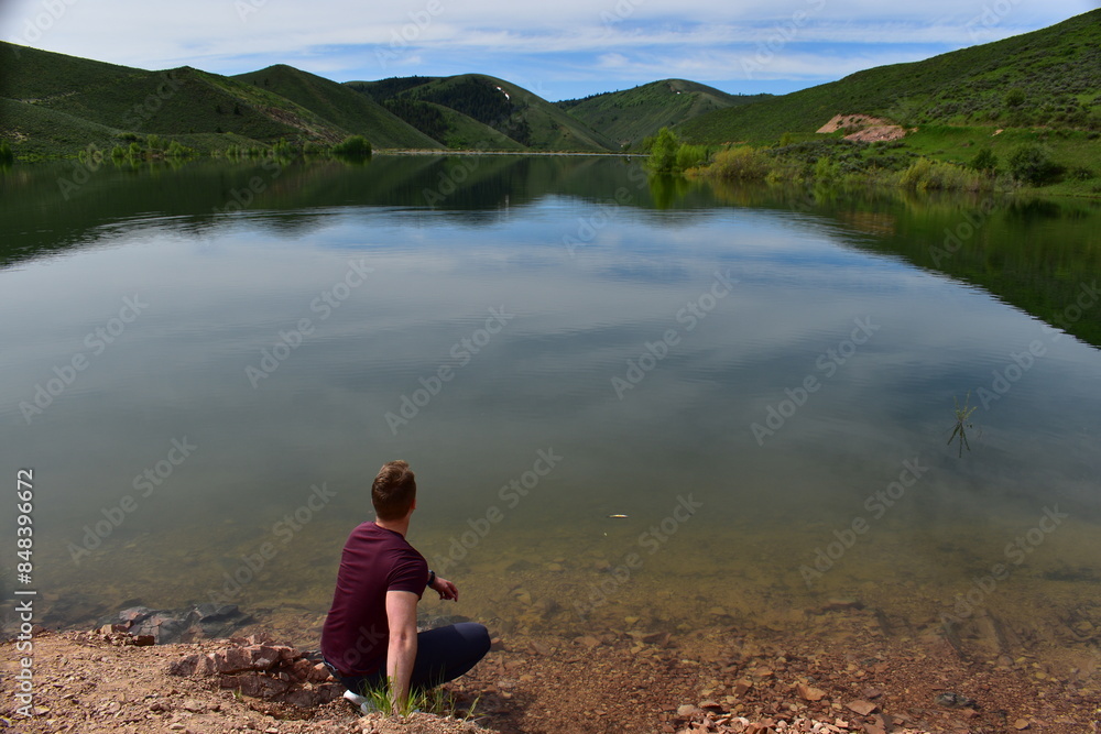 Young athletic man in a bordeaux t-shirt crouching at the shore of Montpellier Reservoir and looking at the still water Young athletic man in a bordeaux t-shirt crouching at the shore of Montpellier Reservoir and looking at the still water