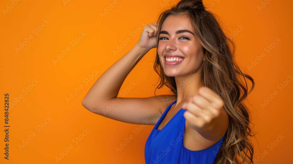 Beautiful young woman in a blue dress before a solid orange colored background. She is in the side of the image, and and show her fist. Beautiful young woman in a blue dress before a solid orange colored background. She is in the side of the image, and and show her fist.