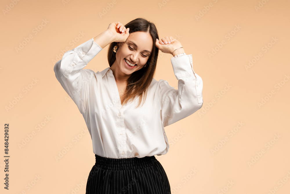 Happy young woman closing eyes dancing holding hands up, isolated on beige background Happy young woman closing eyes dancing holding hands up, isolated on beige background