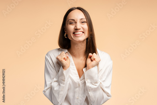 Smiling young woman celebrating victory in winner position over isolated beige background photo