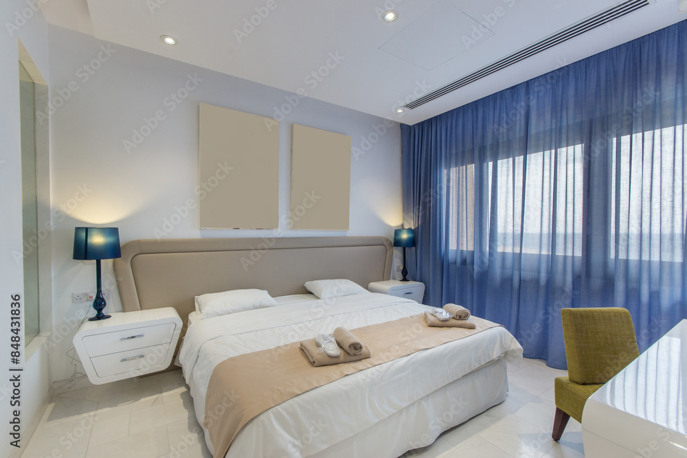 Fototapeta premium Cozy bright bedroom of the hotel with a wide bed and a large window.