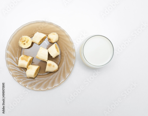Sliced ​​banana in a plate with a glass of milk or yogurt. Fresh banana in the kitchen in a black plate.