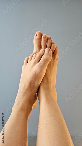 Female feet rubbing against each other, raised up, photograph on a gray background