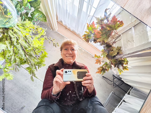 A selfie taken in a mirror, the subject is a woman in her home, with plants in the background